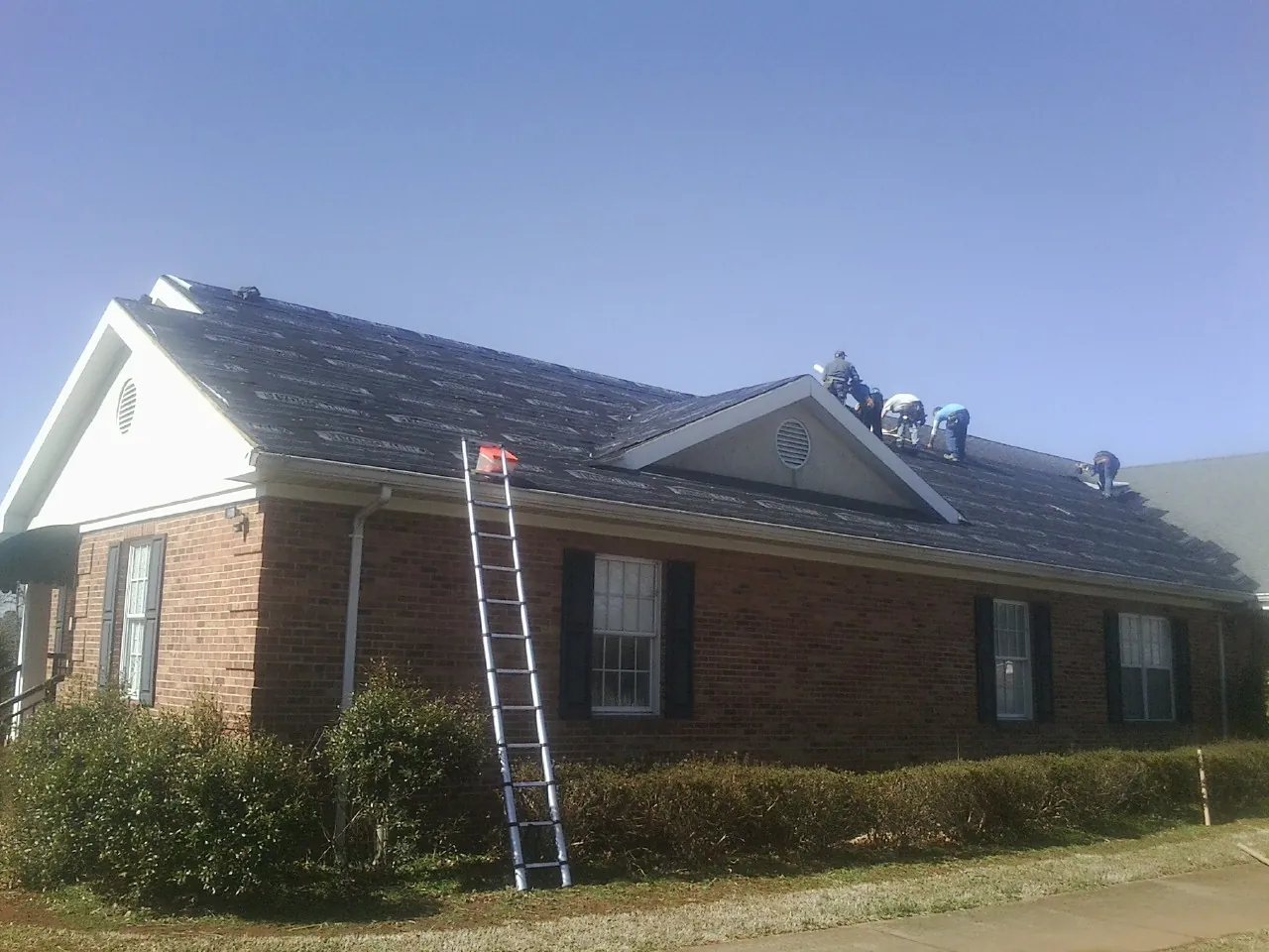 Crew tearing shingles off a brick ranch roof with a ladder set — Metal Roof Repair work by our crew in Panama