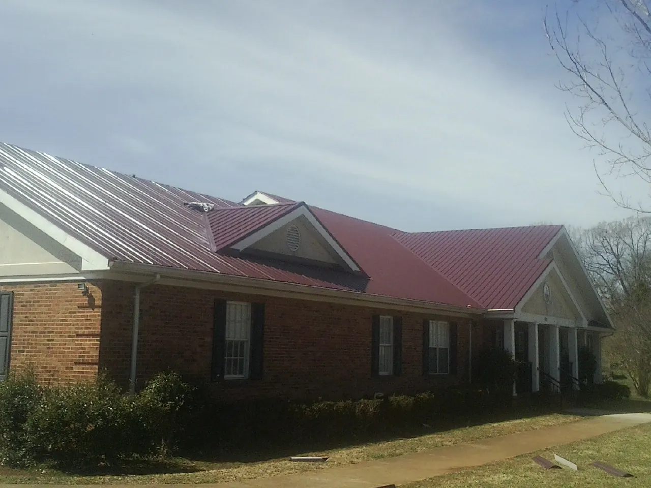 Red metal roof with gabled entries on a long brick building, from a Hail Damage Roof Repair job in Panama