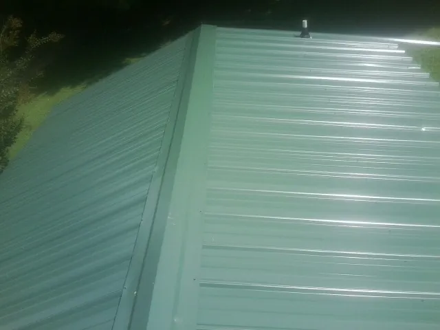 New green metal panels meeting at the ridge of a roof — Flat Roof Repair work by our crew in Panama