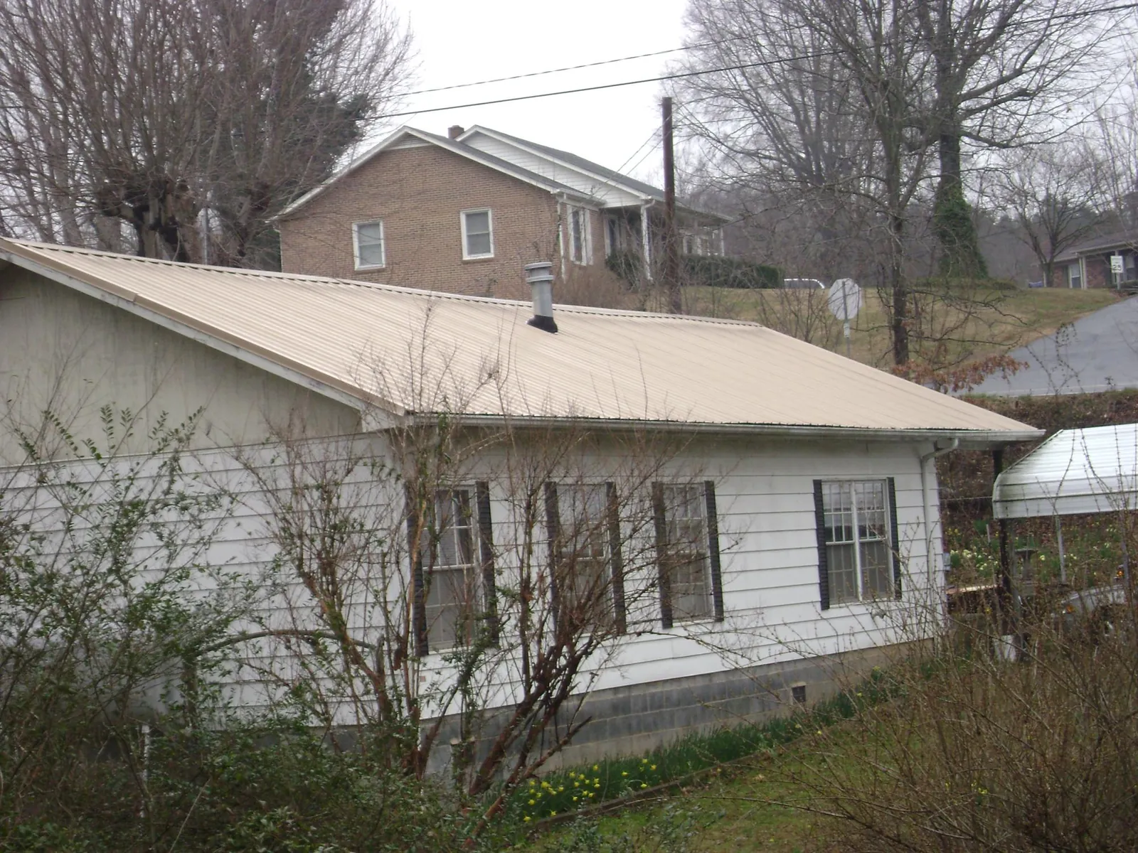 Tan metal roof on a white sided house set into a hillside — Commercial Roofing by Roofing Brothers in Panama